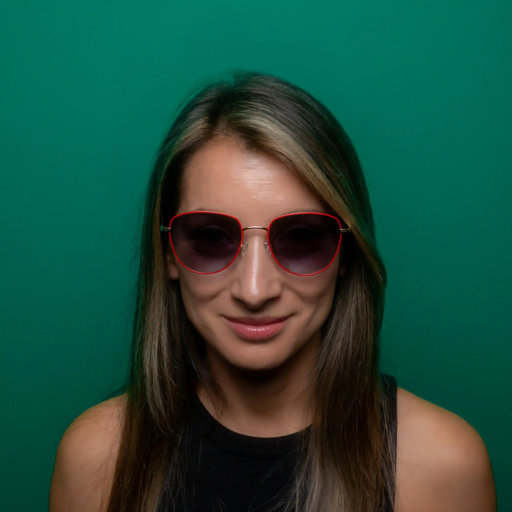 Woman wearing red framed sunglasses with blue lenses standing in front of a tile background