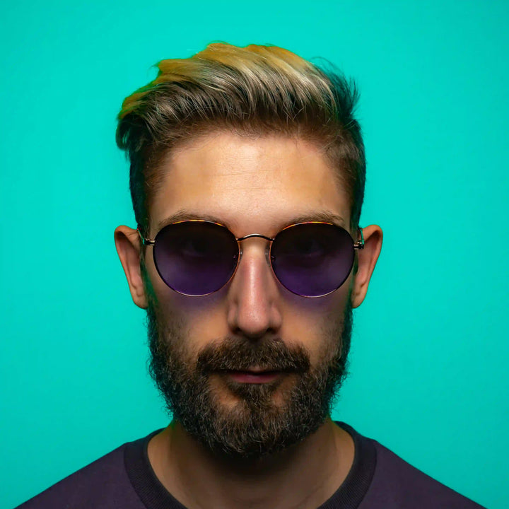 Man wearing tiger sunglasses with blue lenses in front of a teal background